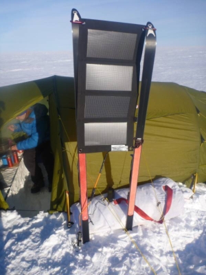 Solar cell panel fastened between two cross country skis. Tent in the background.